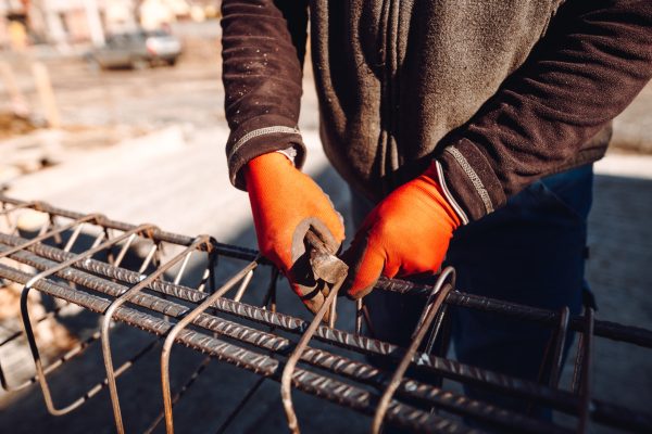 Male construction worker hands securing steel bars with wire rod for reinforcement of concrete